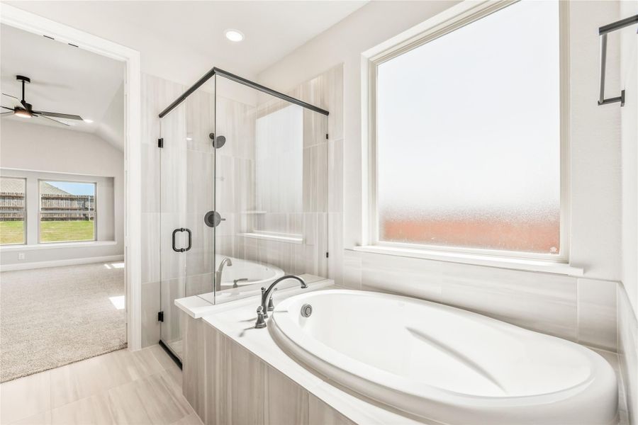 Ensuite bathroom with soaking tub, glass walk-in shower, and large frosted window next to carpeted bedroom Ensuite bathroom with soaking tub, glass walk-in shower, and large frosted window next to carpeted bedroom