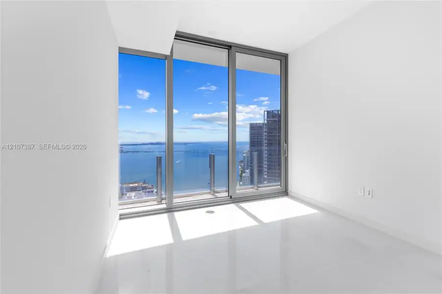 Floor-to-ceiling sliding glass doors, polished tile flooring, and integrated balcony with glass railing showcasing maritime and urban scenery