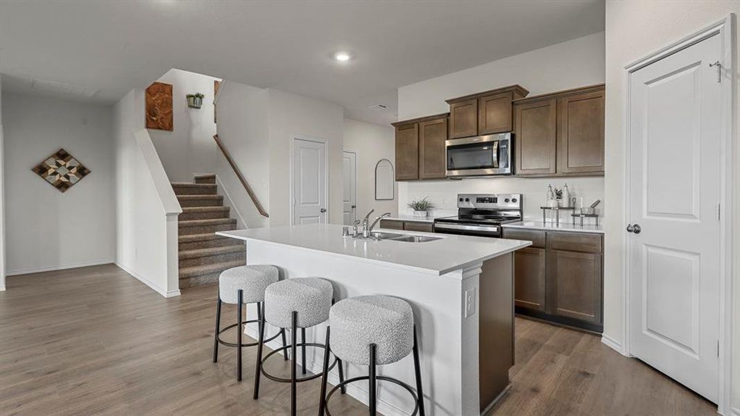 Kitchen with a breakfast bar, stainless steel appliances, a center island with sink, dark wood finished floors, and dark wood finish cabinets