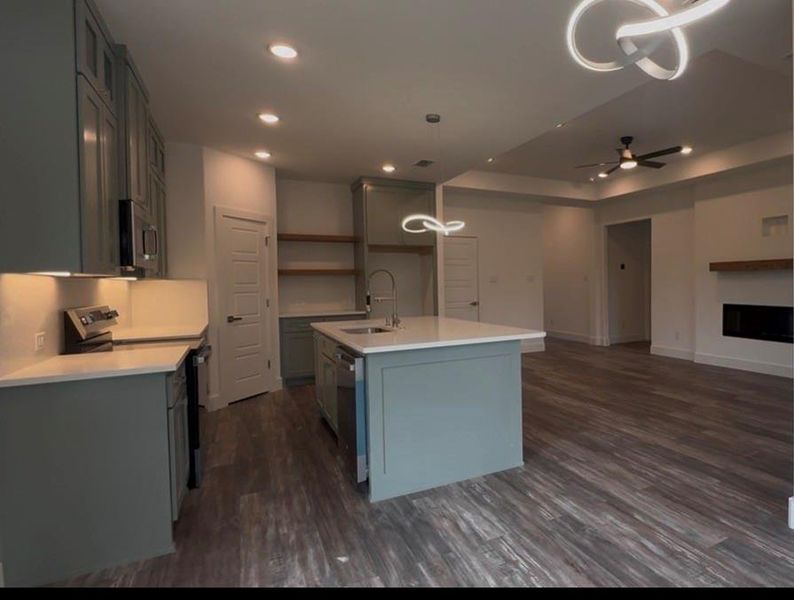 Open-concept kitchen featuring sage cabinetry, a central island with sink, white countertops, stainless steel appliances, and recessed lighting