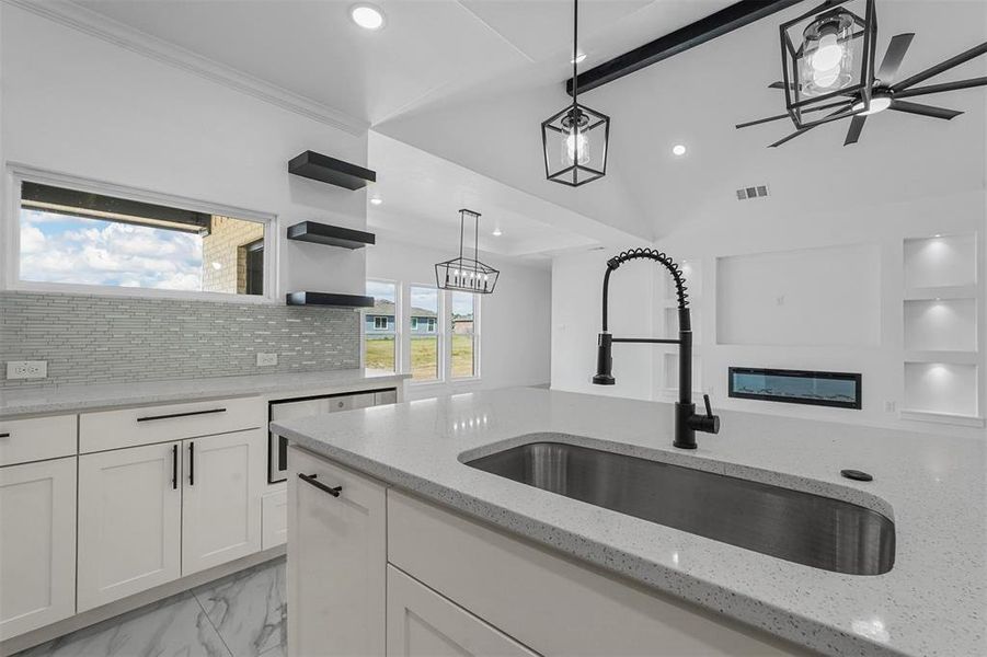 Kitchen with hanging light fixtures, light stone counters, white cabinets, ceiling fan, and sink