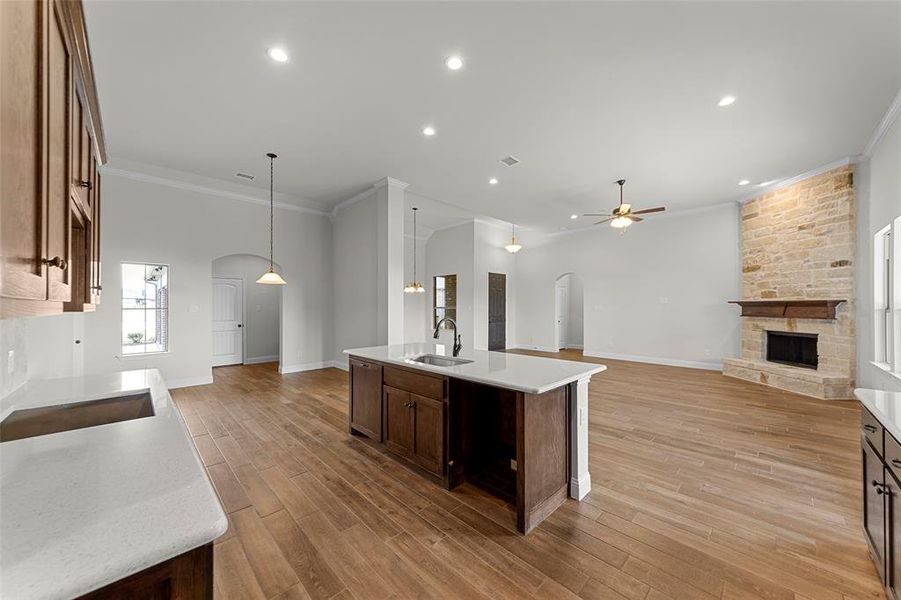 Kitchen with ceiling fan, sink, hanging light fixtures, a fireplace, and a center island with sink