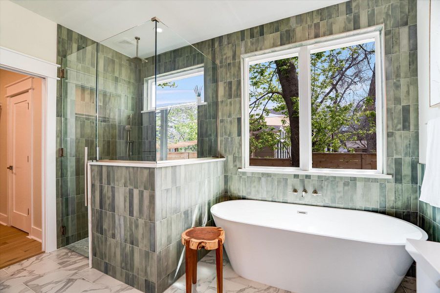 The bathroom features a spacious glass-enclosed shower, a large white freestanding soaking tub, and a window providing natural light The bathroom features a spacious glass-enclosed shower, a large white freestanding soaking tub, and a window providing natural light
