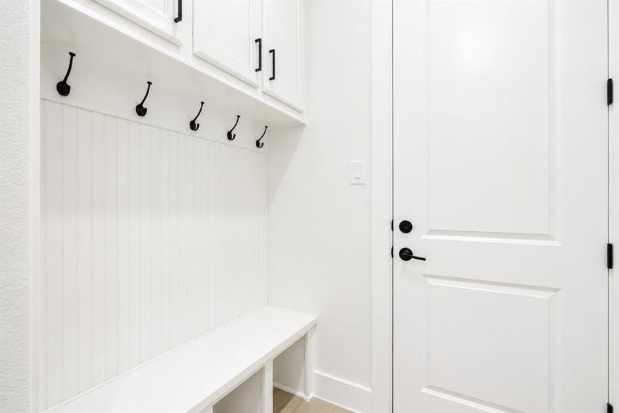 Built-in mudroom bench with beadboard backing, overhead cabinetry, and black hardware