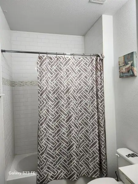 Full bath featuring a textured wall, a textured ceiling, and shower / bath combo