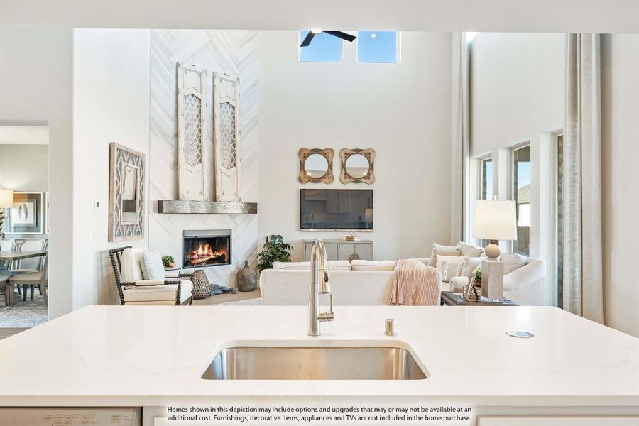 Open-concept living area with kitchen island sink, fireplace, high ceilings, and white furnishings visible from kitchen