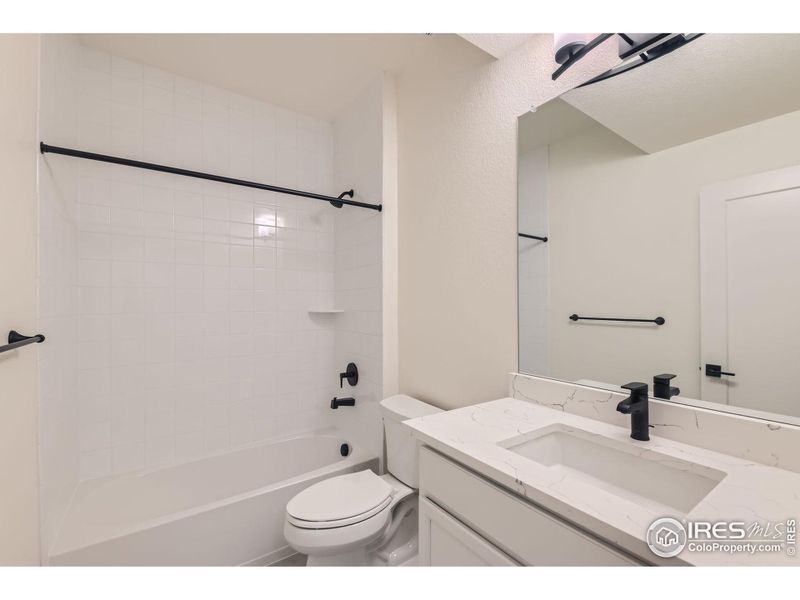 Full bathroom in basement with tile floor, tile surround, quartz counters.