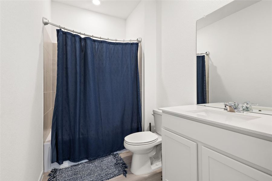 This bathroom features a clean, modern design with a white vanity, a large mirror, and a bathtub with a navy blue shower curtain. The space is well-lit with a minimalist aesthetic.