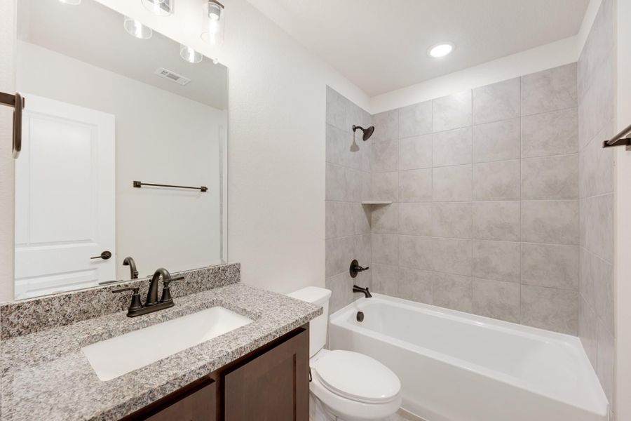 Bathroom with granite countertop vanity, white tub-shower combo with gray tile surround, and dark bronze fixtures