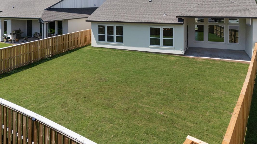 Expansive backyard featuring a large green lawn, full privacy fencing, and a covered concrete patio