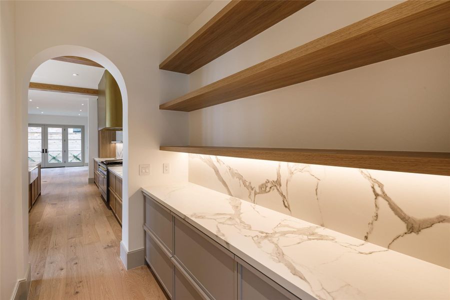 Tucked between the dining room and kitchen, this butler's pantry earns its keep. Floating wood shelves, illuminated marble-look backsplash and countertops, and generous cabinetry make entertaining feel considerably more effortless.
