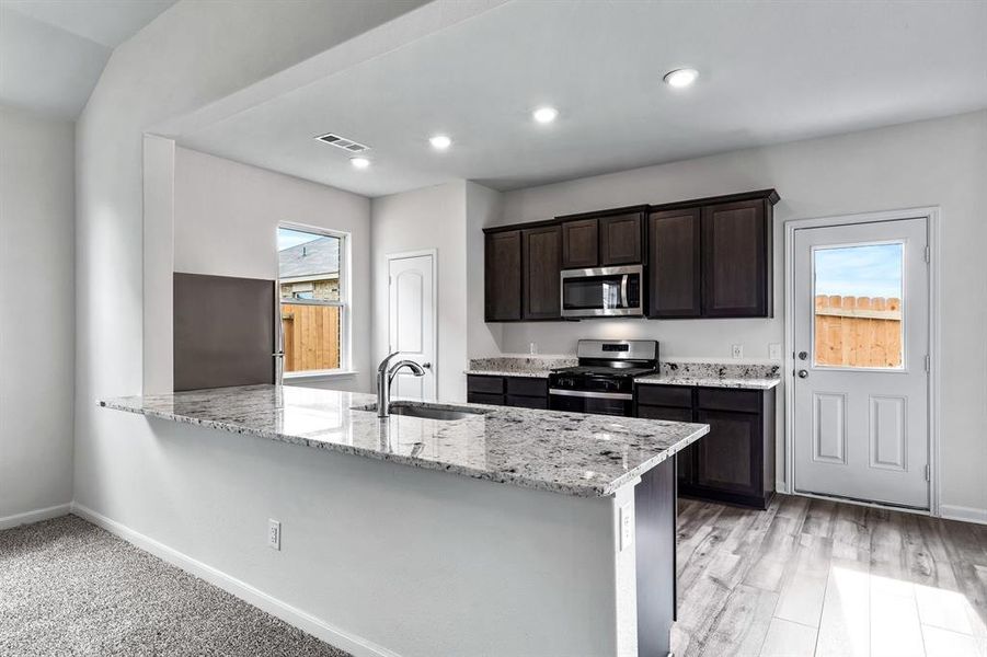 Kitchen featuring appliances with stainless steel finishes, light hardwood / wood-style flooring, sink, kitchen peninsula, and light stone countertops