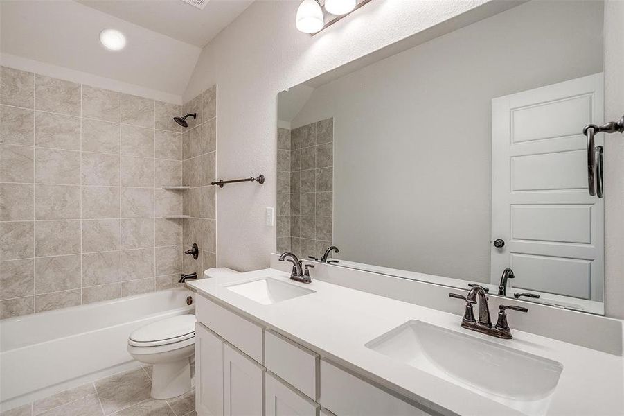 Full bathroom featuring tiled shower / bath, dual vanity, vaulted ceiling, toilet, and tile patterned flooring