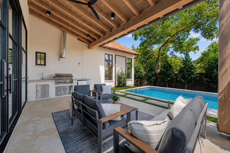 An inviting covered patio featuring a built-in outdoor kitchen overlooking a sparkling pool.