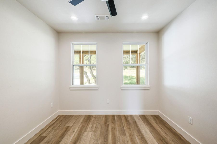 Light-filled room with dual windows, wood-look flooring, and ceiling fan—ideal as a bedroom or study. Light-filled room with dual windows, wood-look flooring, and ceiling fan—ideal as a bedroom or study.