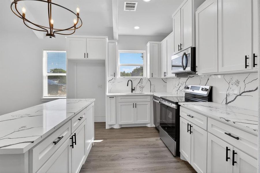 Modern kitchen featuring white shaker-style cabinetry, dark hardware, and light countertops with dark veining