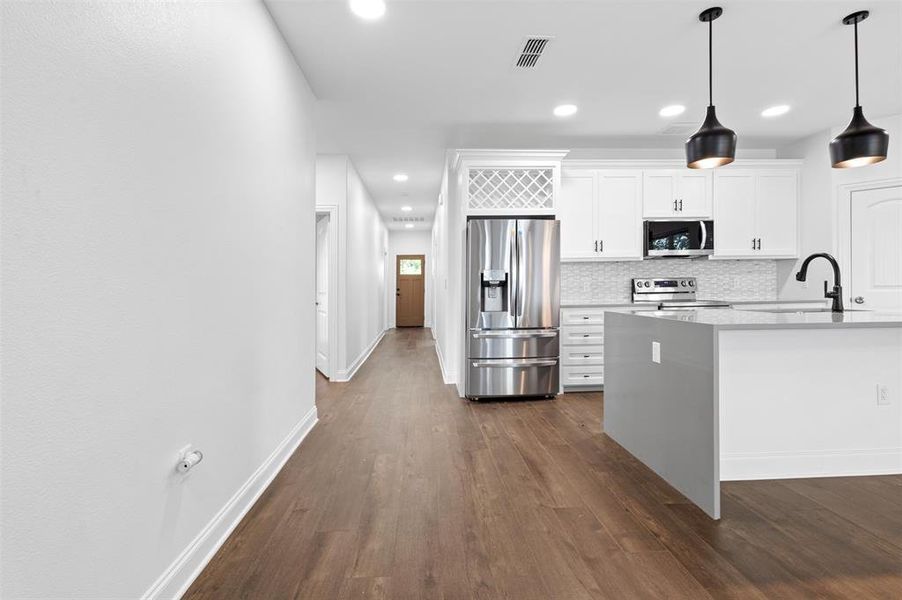 Kitchen with appliances with stainless steel finishes, white cabinets, dark wood-style floors, light stone countertops, and hanging light fixtures