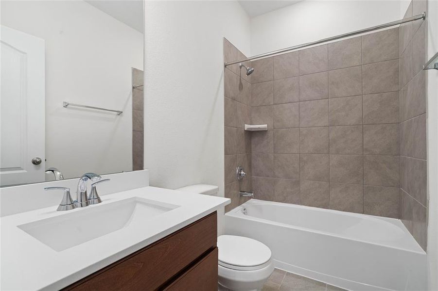 Secondary bath features tile flooring, tub/shower combo with tile surround, stained wood cabinets, beautiful light countertops, mirror, sleek fixtures and modern finishes.