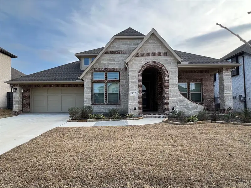 French provincial home featuring a shingled roof, concrete driveway, a two-car garage, stone facade, brick siding, and a front lawn French provincial home featuring a shingled roof, concrete driveway, a two-car garage, stone facade, brick siding, and a front lawn