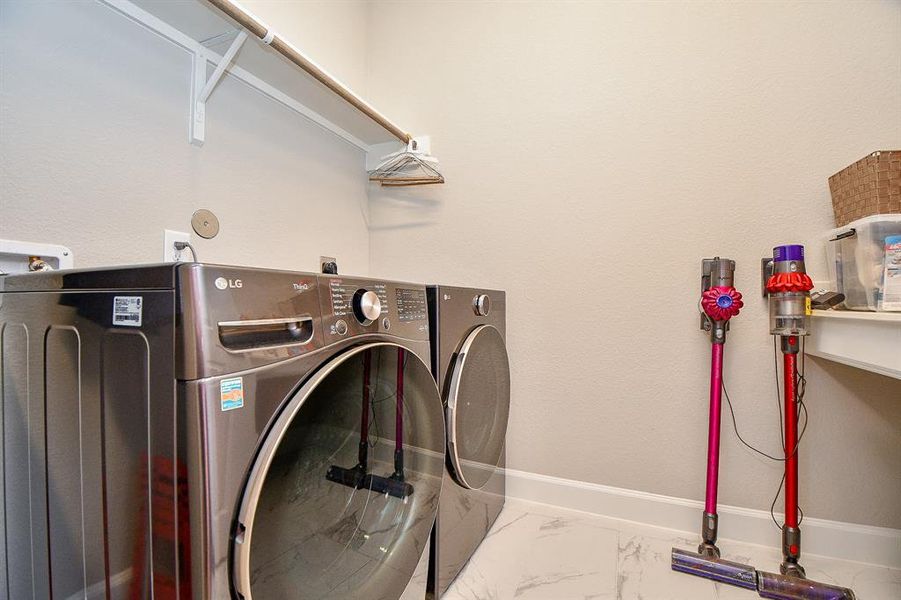 This photo shows a modern laundry room featuring a sleek washer and dryer set, wall-mounted storage shelf, and ample space for additional cleaning tools.