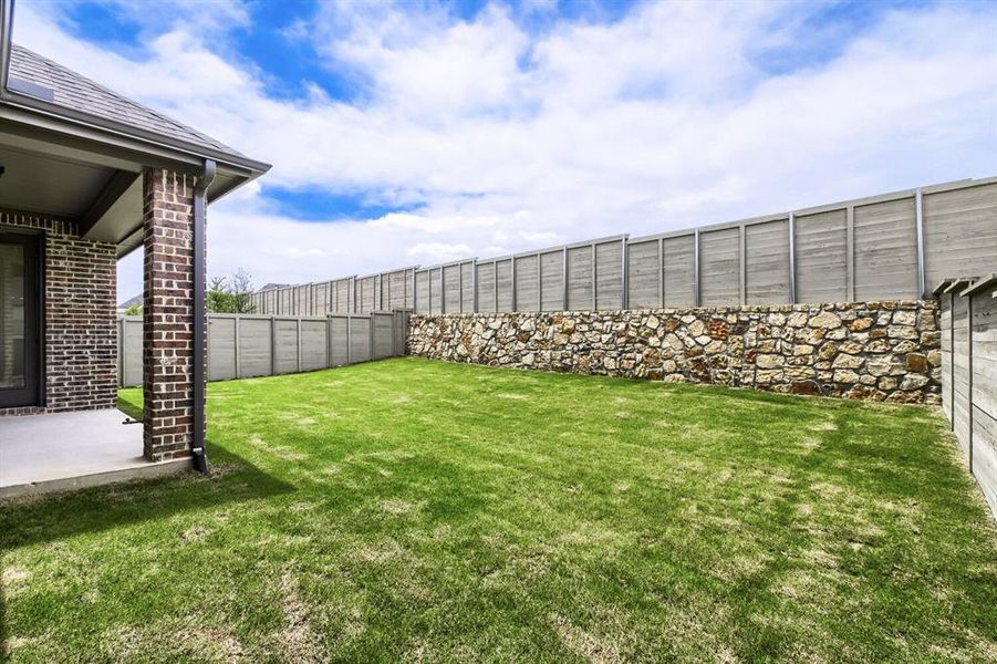 Expansive green lawn with a stone retaining wall and privacy fencing