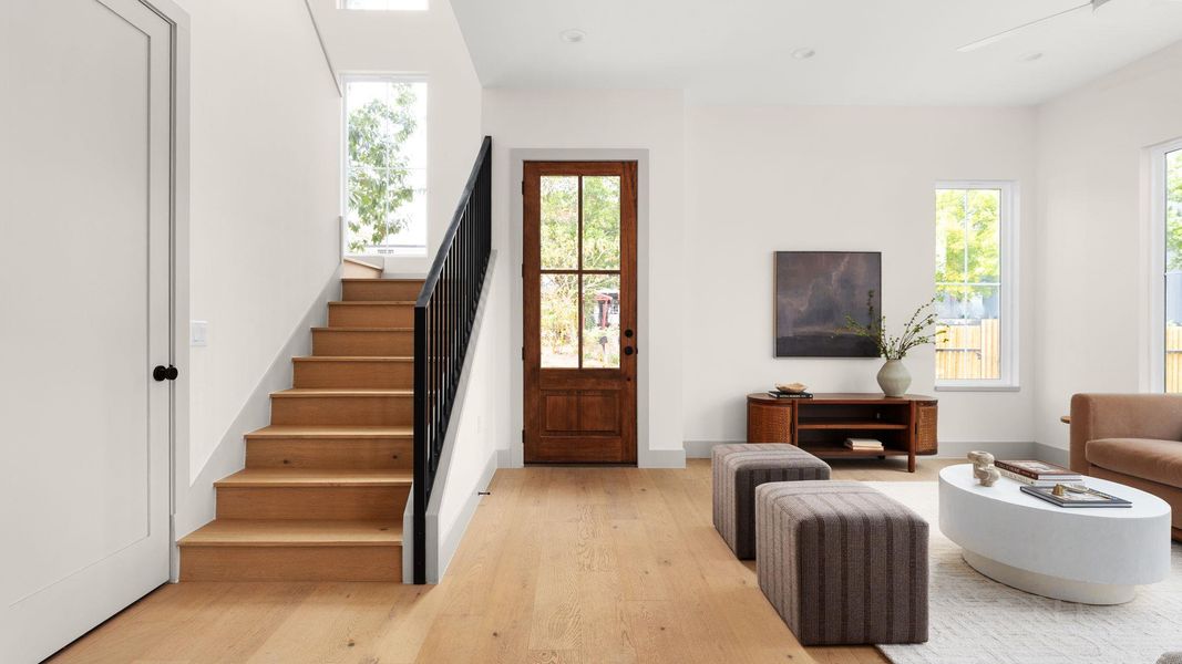 Living area with stairs, light wood-style floors, and healthy amount of natural light