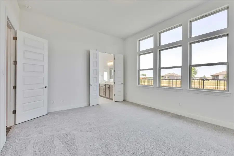 Unfurnished bedroom featuring light colored carpet, baseboards, and connected bathroom Unfurnished bedroom featuring light colored carpet, baseboards, and connected bathroom