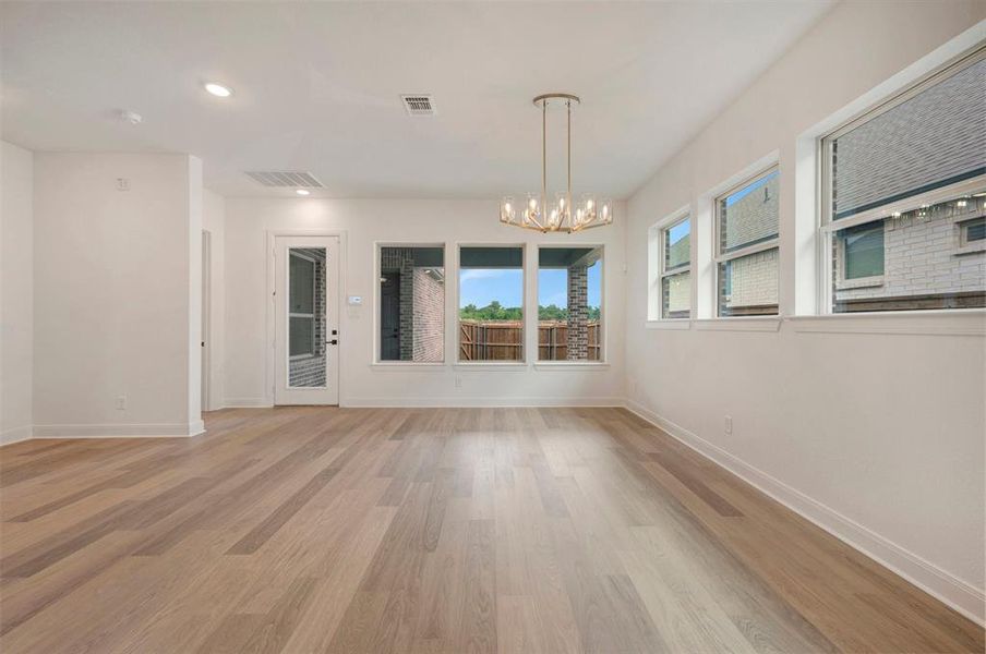 Spacious room featuring light-colored hardwood floors, white walls, and a modern chandelier