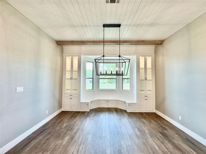 Unfurnished dining area featuring dark wood-style flooring, a chandelier, baseboards, and wooden ceiling with exposed beams