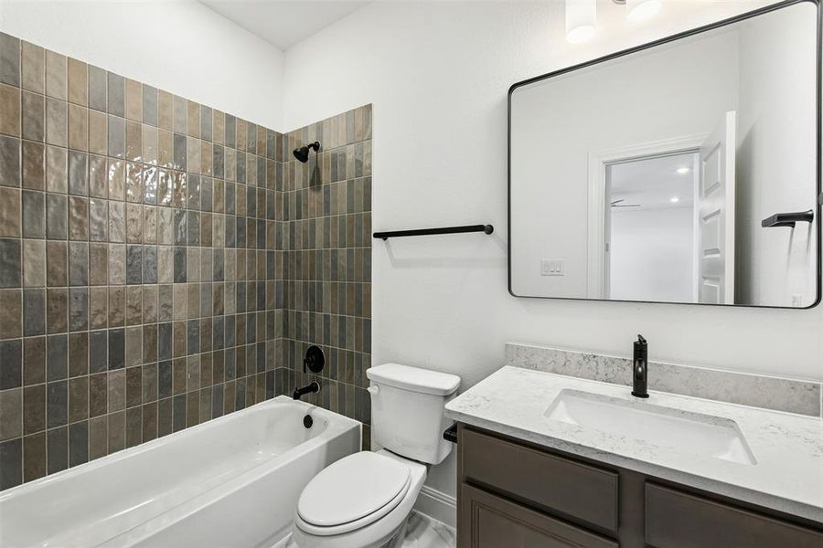 Bathroom featuring a tiled bath/shower combination with matte black fixtures, a white vanity with a rectangular undermount sink, a stone countertop, and a framed mirror