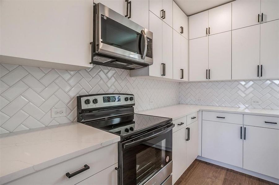 Kitchen featuring light stone countertops, white cabinetry, stainless steel appliances, backsplash, and dark hardwood / wood-style floors Kitchen featuring light stone countertops, white cabinetry, stainless steel appliances, backsplash, and dark hardwood / wood-style floors