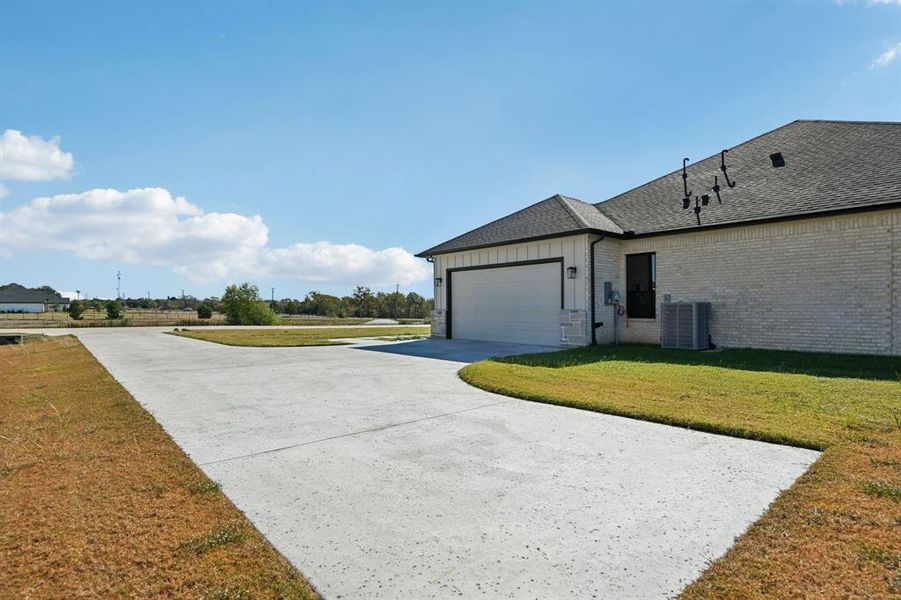 View of property exterior featuring a lawn, concrete driveway, roof with shingles, brick siding, and board and batten siding View of property exterior featuring a lawn, concrete driveway, roof with shingles, brick siding, and board and batten siding