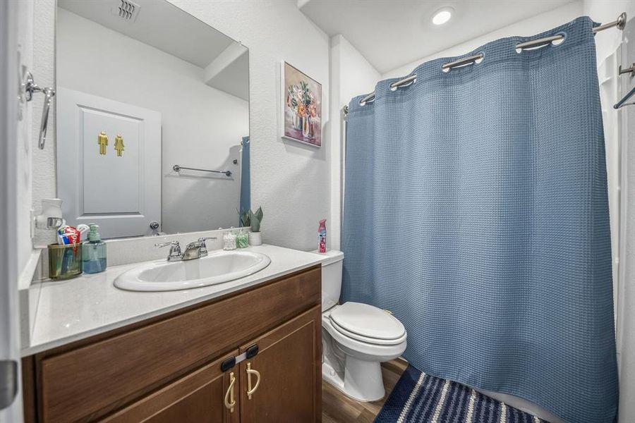 Bathroom featuring a wood-finish vanity with a single basin sink, white countertop, and chrome faucet Bathroom featuring a wood-finish vanity with a single basin sink, white countertop, and chrome faucet