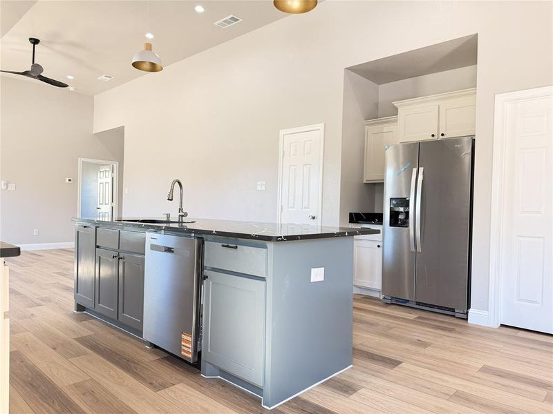 Kitchen featuring stainless steel appliances, a ceiling fan, light wood-type flooring, a high ceiling, and an island with sink