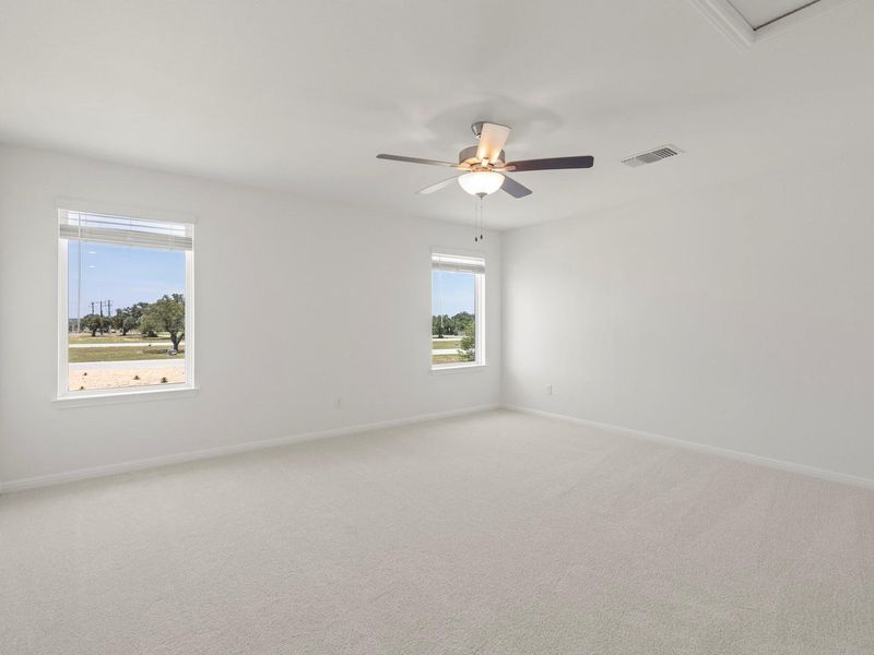 A well-lit, neutral-toned room features broad windows, plush carpet, and a ceiling fan.