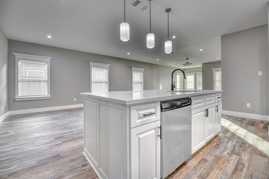 Kitchen featuring white cabinetry, light stone countertops, dishwasher, open floor plan, and a kitchen island with sink
