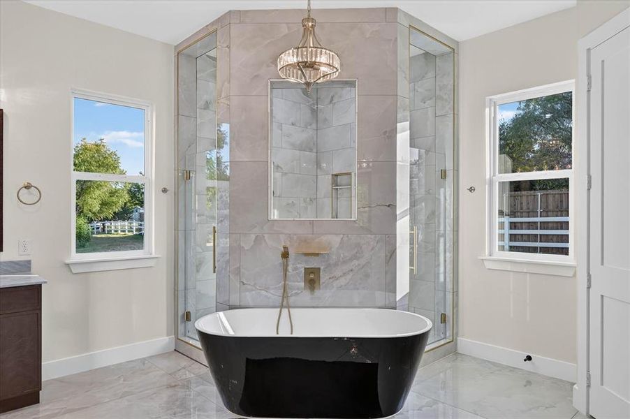 Freestanding black soaking tub with wall-mounted brass faucet, framed by a spacious glass-enclosed shower with tiled walls Freestanding black soaking tub with wall-mounted brass faucet, framed by a spacious glass-enclosed shower with tiled walls