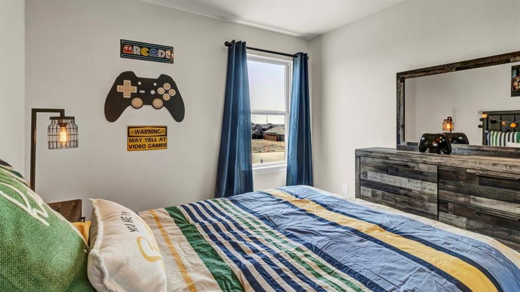 Bedroom featuring a single window with blue drapes, a wood-finish dresser with a mirror, and a wall-mounted industrial style light fixture Bedroom featuring a single window with blue drapes, a wood-finish dresser with a mirror, and a wall-mounted industrial style light fixture