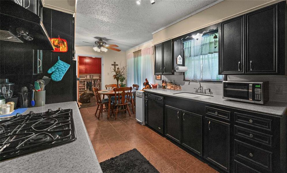 Kitchen with dark cabinetry, black appliances, extractor fan, a ceiling fan, and a textured ceiling