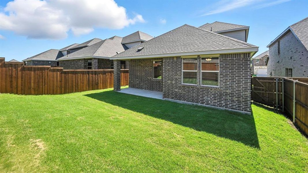 Back of property with a fenced backyard, brick siding, a patio area, and roof with shingles