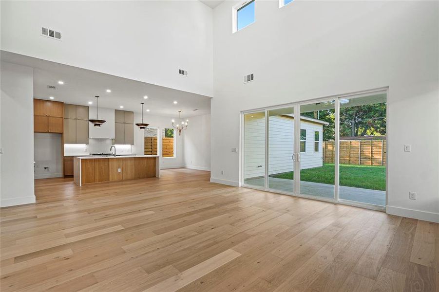 Unfurnished living room featuring light wood-type flooring, a chandelier, and a towering ceiling