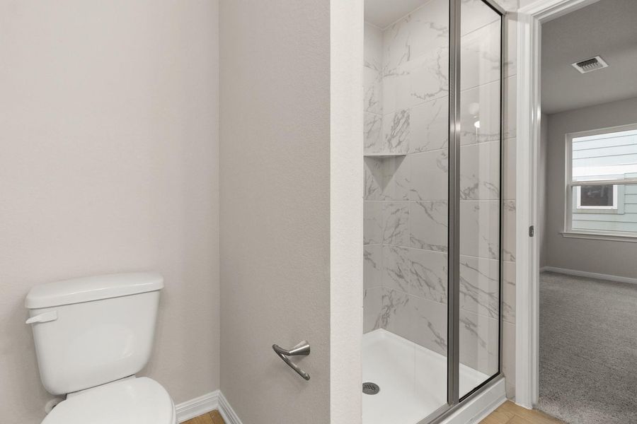 The bathroom features a toilet and a shower with a glass enclosure and marble-patterned tile work