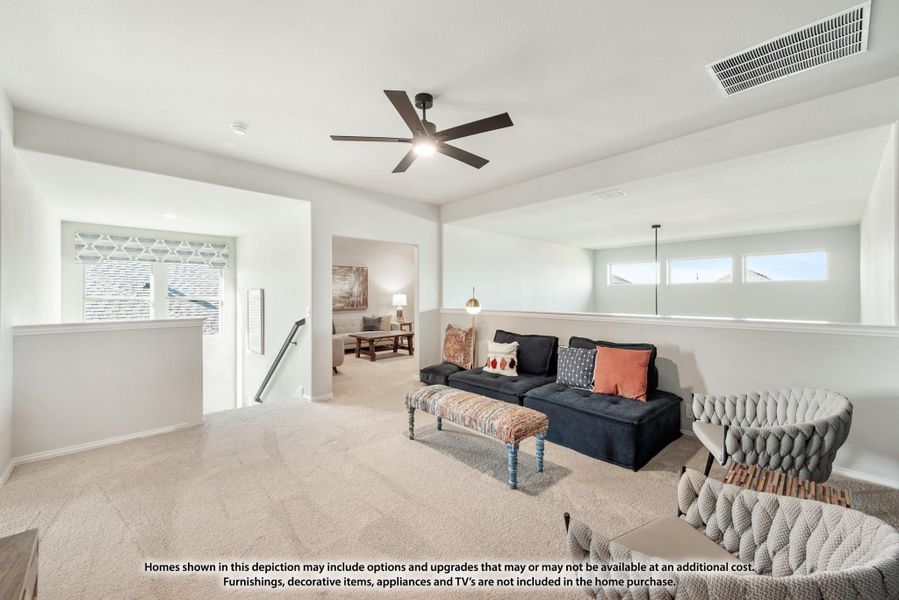 Upstairs loft sitting area with carpet, ceiling fan, dark sofa, and open staircase landing nearby