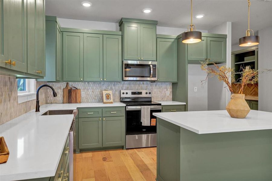 Kitchen with green cabinetry, appliances with stainless steel finishes, light wood finished floors, light stone countertops, and decorative backsplash