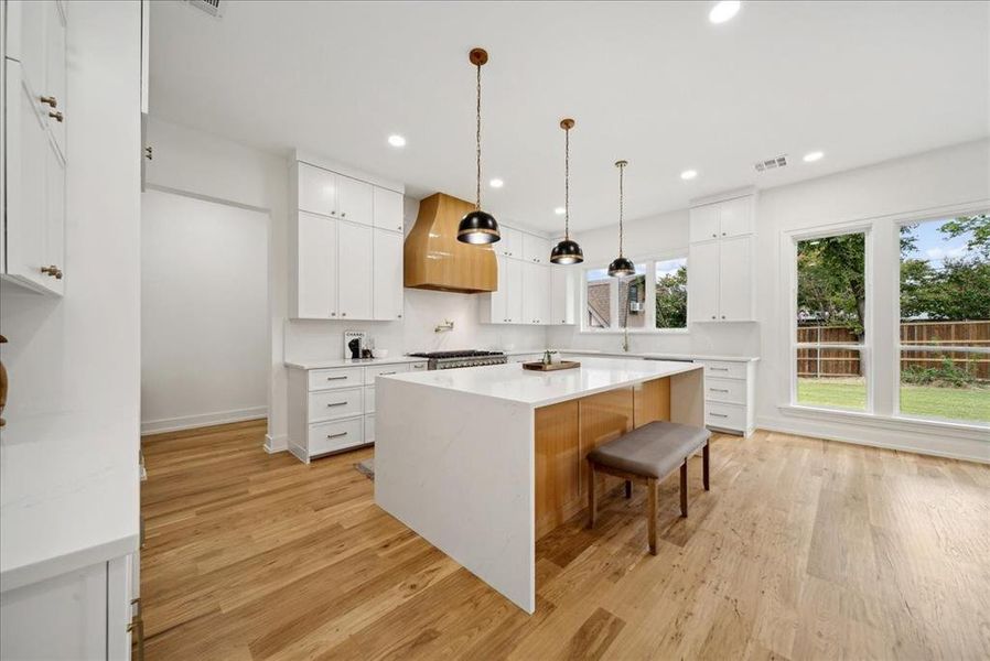 Kitchen with white cabinets, decorative light fixtures, a kitchen island, light wood-type flooring, and a kitchen breakfast bar