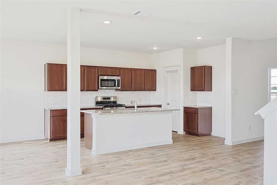 Kitchen featuring sink, light wood-type flooring, stainless steel appliances, and a kitchen island with sink