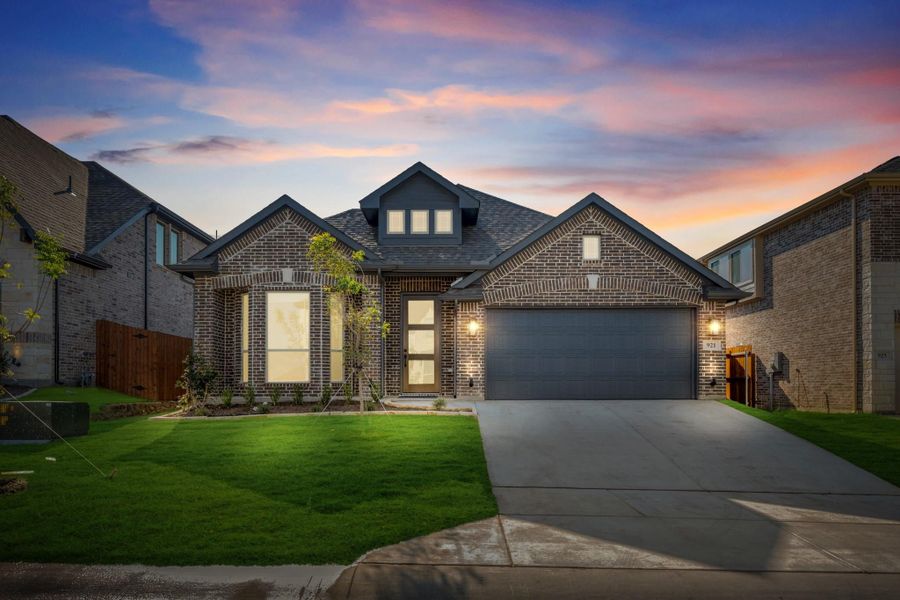 Single-story brick home with dark roof, two-car garage, and green front lawn at dusk Single-story brick home with dark roof, two-car garage, and green front lawn at dusk