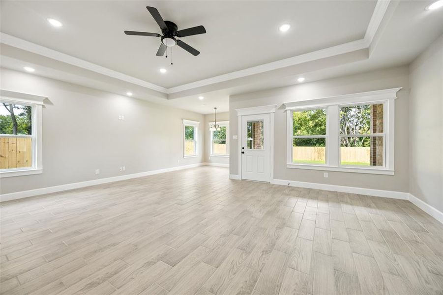 Unfurnished living room featuring healthy amount of natural light, recessed lighting, ornamental molding, a tray ceiling, and light wood-style floors Unfurnished living room featuring healthy amount of natural light, recessed lighting, ornamental molding, a tray ceiling, and light wood-style floors