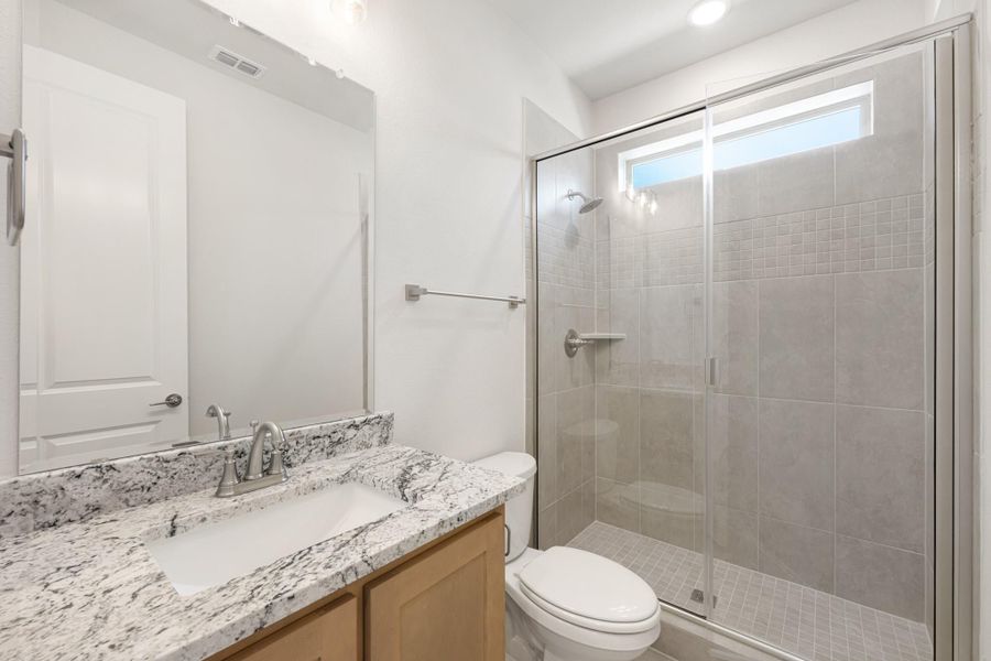 Bathroom with granite countertop vanity, glass-enclosed tile shower, and toilet with white walls
