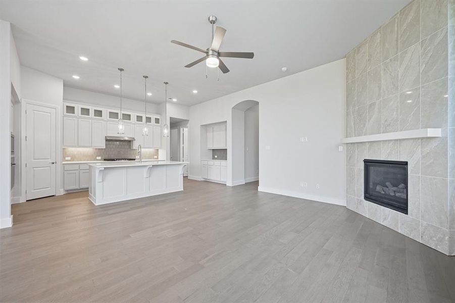 Unfurnished living room with arched walkways, a tile fireplace, ceiling fan, light wood-type flooring, and recessed lighting Unfurnished living room with arched walkways, a tile fireplace, ceiling fan, light wood-type flooring, and recessed lighting